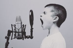 A boy seemingly screaming into a microphone. Build your brand based on personality and voice.