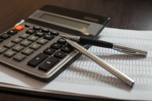 A calculator on a desk with two pens. Starting your accounting firm cam be rewarding.