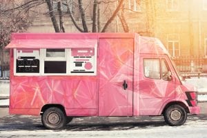 A pink food truck with a food truck logo design visible in the window.