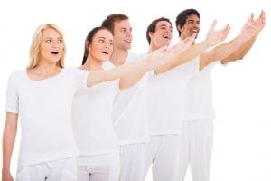 Five people in a row holding up their left arm, singing. A church performance group