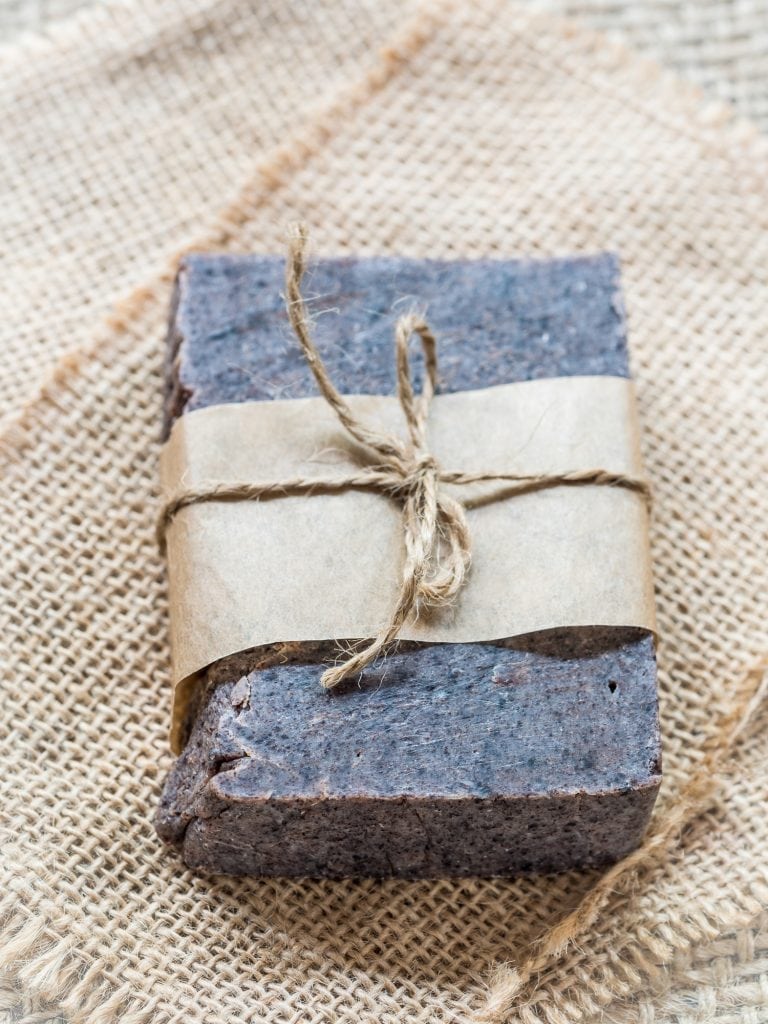 a bar of blue/grey all-natural soap wrapped with parchment paper and tied with a tweed bow 
