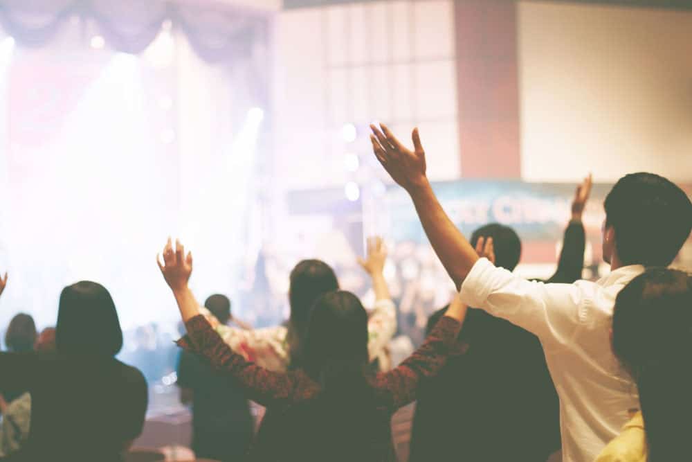 People raising their hands up towards the sky inside a religious place. Marketing to churches is like marketing to any other business. 