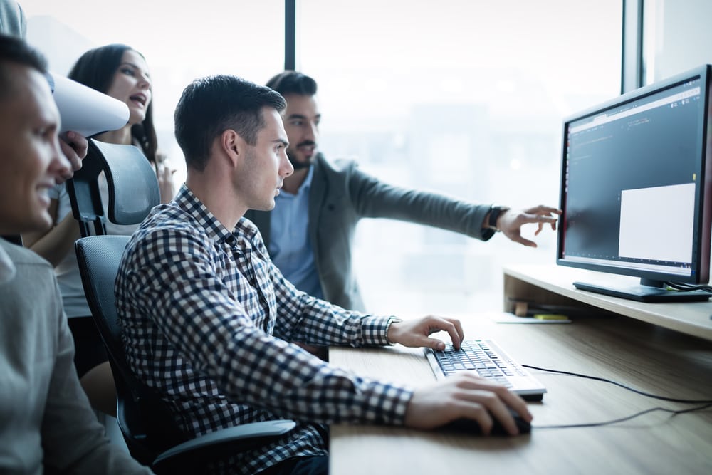 Four people talking around a computer screen. Planning to start a computer programming business