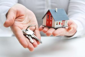 A hand holding a little house and the other hand holding a set of keys to symbolise marketing and starting a real estate business. 