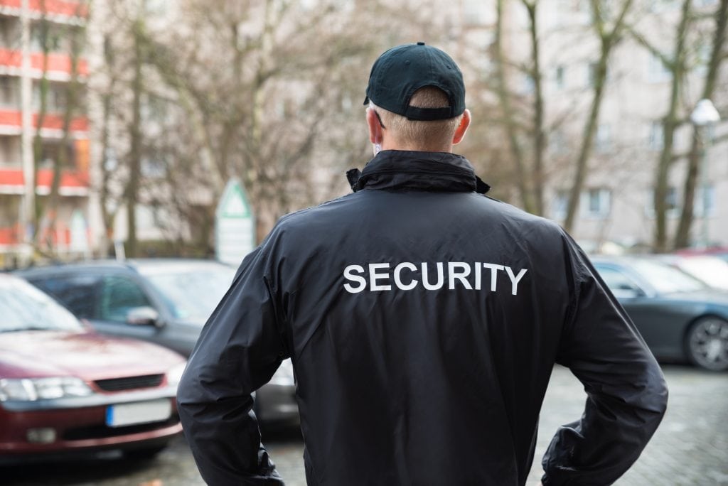 Male security guard standing at a parking lot and observing cars 