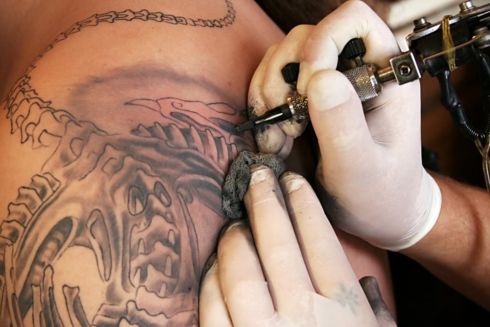 Artist making a tattoo in the shape of a skeleton. Image to illustrate how to start a tattoo shop with a tattoo logo design.