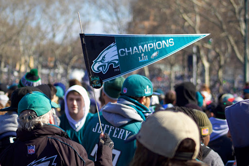 A man walking in a crowd of people wearing Philadelphia Eagles gear holding a sign that shows that the Eagles were the superbowl champions in Superbowl LII.