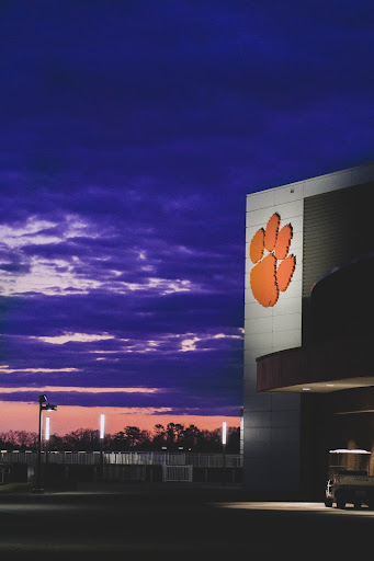 An athletic building with the Clemson Tigers’ orange paw print logo illuminated in front of a purple sunset.