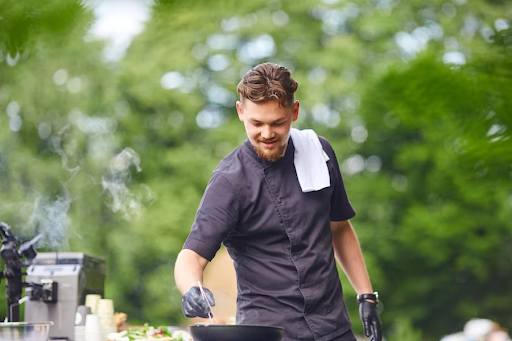 A guy with gloves using a BBQ, cooking something.