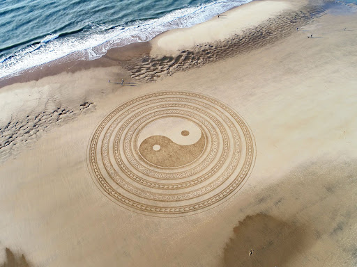 The yin and yang logo painted in the sand on a beach