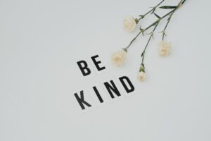 Be kind on a sign with some white flowers on the right hand side