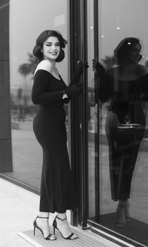 Young Elegant Woman in a Long Black Dress and High Heels Standing by the Window and Smiling Young Elegant Woman in a Long Black Dress and High Heels Standing by the Window and Smiling. Symbolizing classic logo