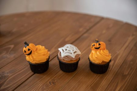 Three Halloween Cupcakes on Brown Wooden Table Three Halloween Cupcakes on Brown Wooden Table. Great Halloween Bakery Logo Ideas
