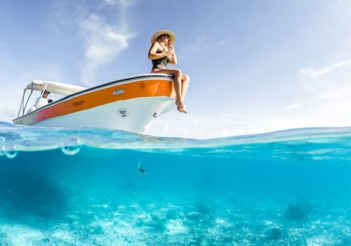 Boat on the crystal clear ocean. A woman is sitting on the deck with her legs hanging out. Perfect summer logo ideas for everyone.