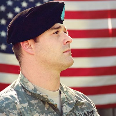 US military man standing proudly with the US flag in the background.