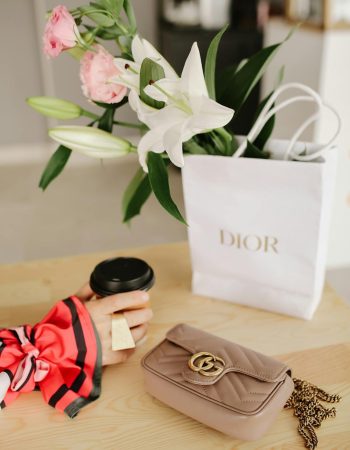 Hand with a Ring, Paper Cup, A luxury brand Gucci Handbag and Flowers in a Shopping Bag