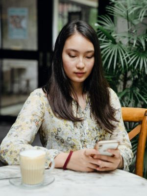 Young attentive Asian woman reading about email logo design ideas on her mobile phone in street cafe