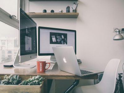 A desk with a coffee cup and a silver MAC computer. Graphic design vs automation is the big questions.